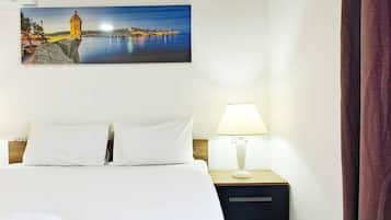 Ein Hotelzimmer mit Bett, Nachttisch, Lampe, einem Gemälde einer Küstenlandschaft und einem Vorhang.
