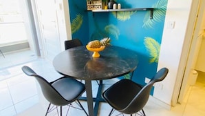 Un comedor con una mesa redonda, cuatro sillas y un centro de mesa con piña.