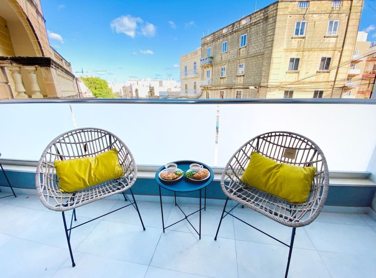 Ein Balkon mit zwei Korbstühlen, einem kleinen runden Tisch und einer Ablage mit Speisen und Getränken.