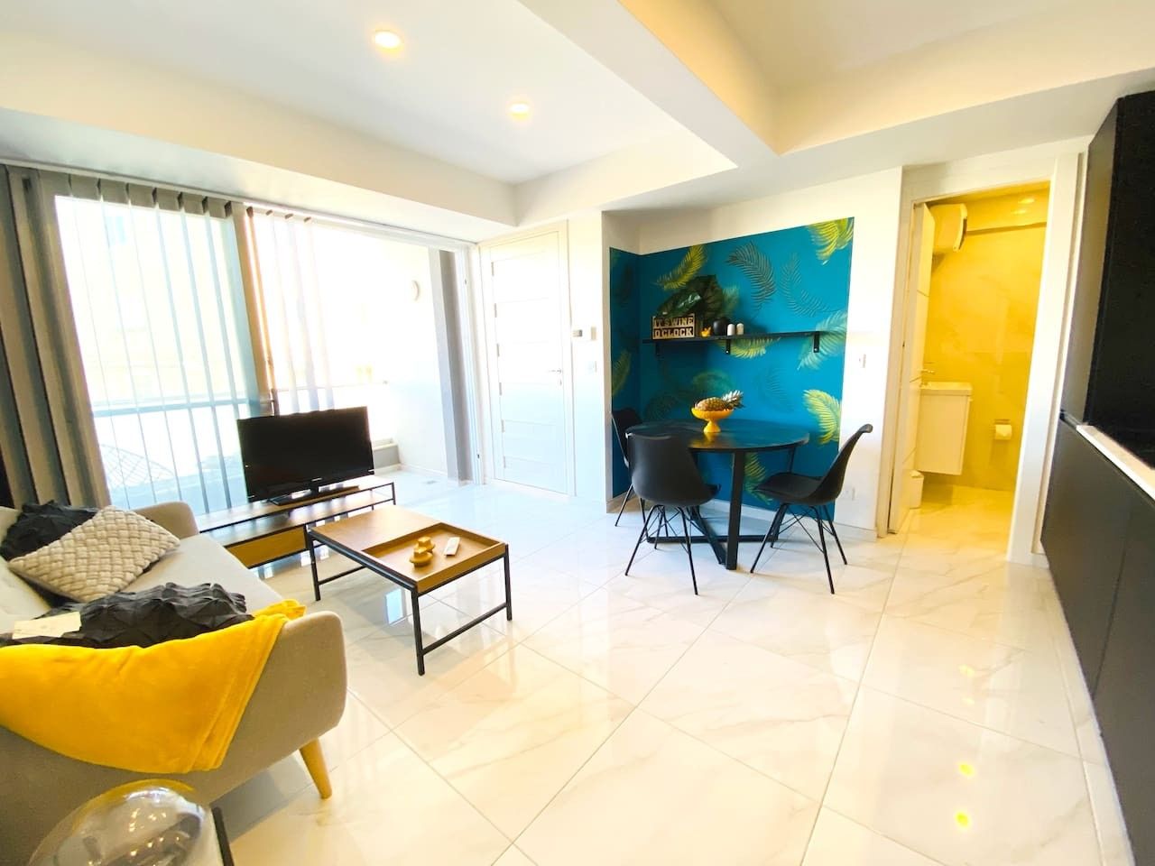 A modern living room with a sofa, coffee table, and a TV. There is a dining area with chairs and a table.