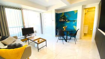 A modern living room with a sofa, coffee table, and a TV. There is a dining area with chairs and a table.