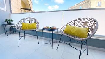Une terrasse avec deux chaises en osier et une petite table, une plante en pot et un bâtiment en arrière-plan.
