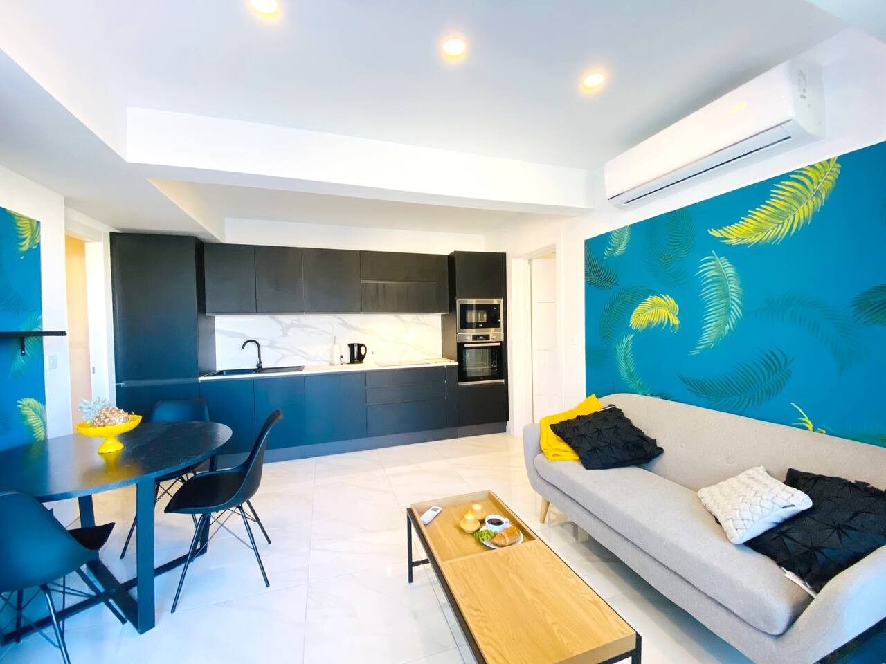 A modern living space with a dining area, a sofa, and a kitchen in the background.