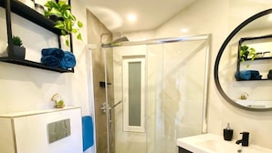 Un baño moderno con ducha de vidrio, inodoro blanco y tocador con espejo.