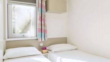 A bedroom with two beds, a window with a curtain, and a small bedside table with a flower vase.
