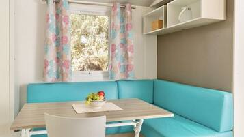 A room with a teal sofa, a small table with a bowl of fruit, and a window with patterned curtains.
