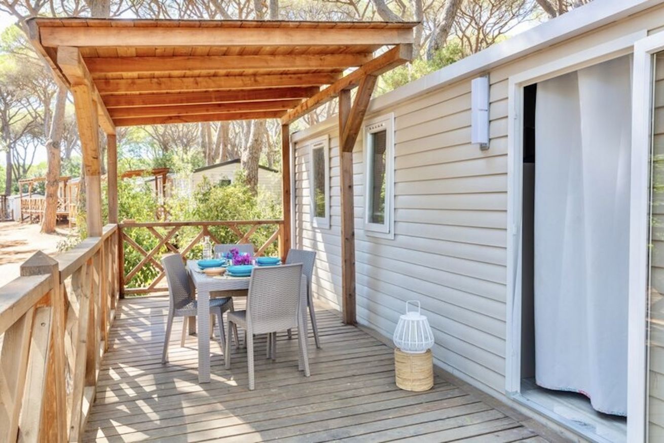 A wooden deck with a table and chairs, a covered area, and a cabin-style building.