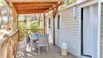 A wooden deck with a table and chairs, a covered area, and a cabin-style building.