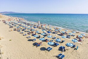 A beach with rows of sun loungers and umbrellas, a lifeguard tower, and the sea in the background.