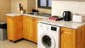 Una cucina compatta con mobili in legno, lavatrice integrata e finestra sopra il lavello.