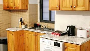 Una cucina compatta con mobili in legno, lavatrice integrata e finestra sopra il lavello.