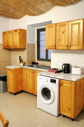 A compact kitchen with wooden cabinets, a built-in washing machine, and a window above the sink. - Valletta Retreat apartment (Valletta)