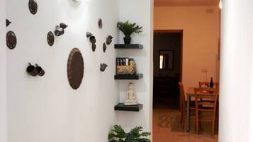 Un corridoio con parete bianca decorata con oggetti ornamentali, una pianta in vaso e un'area pranzo con mobili in legno.
