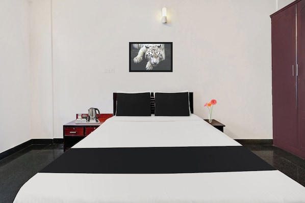 A hotel room with a bed, a nightstand, a red cabinet, a framed picture on the wall, and a vase with flowers.