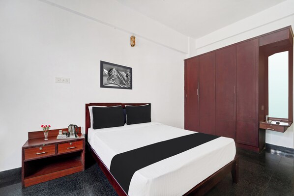 A hotel room with a bed, a bedside table with a tray of items, a wardrobe, and a framed picture on the wall.