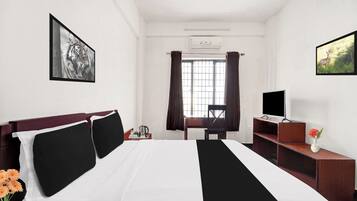 A hotel room with a bed, a desk, a chair, a television, and a window with curtains.