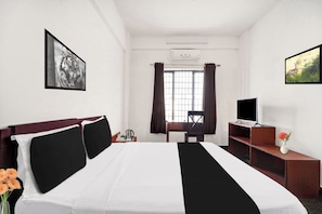 A hotel room with a bed, a desk, a chair, a television, and a window with curtains.