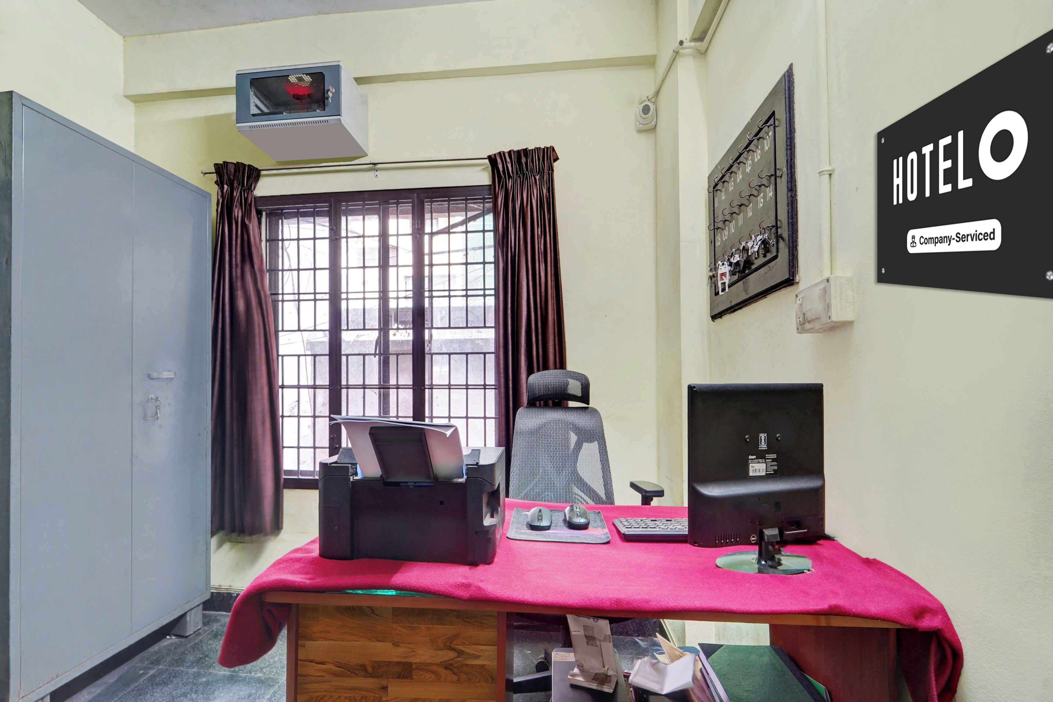 A hotel room with a desk, chair, computer, and a window with curtains.
