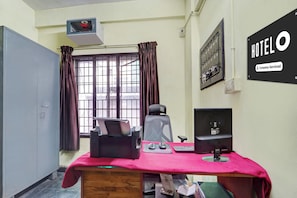 A hotel room with a desk, chair, computer, and a window with curtains.