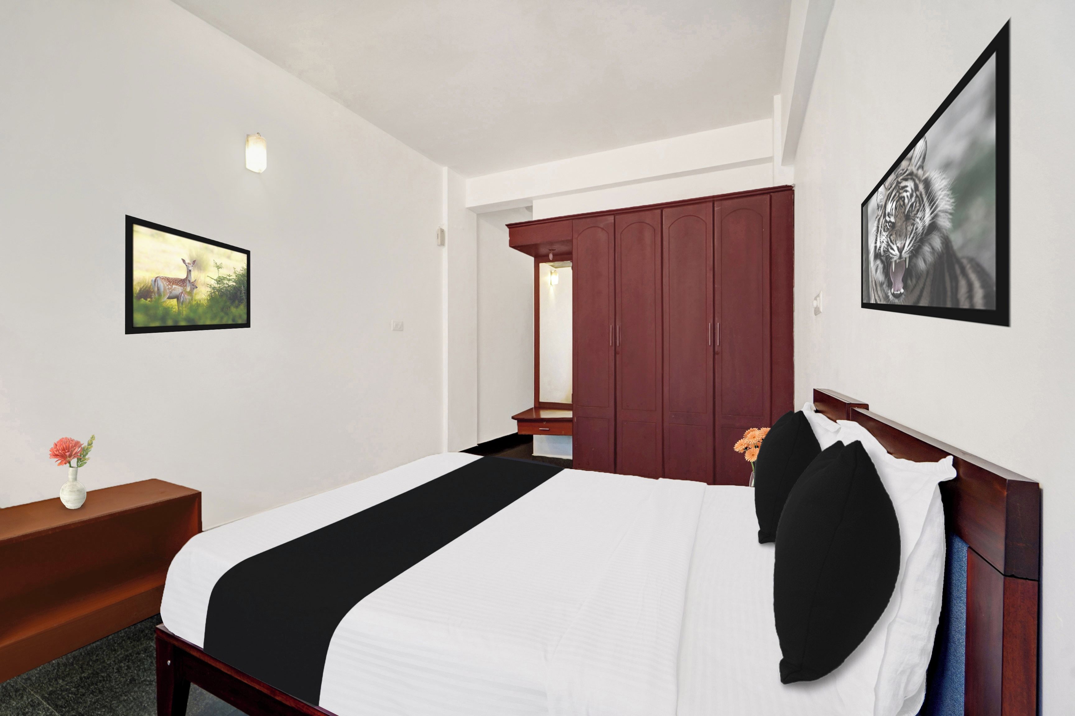 A hotel room with a bed, a wardrobe, a desk with a vase of flowers, and two framed pictures on the walls.