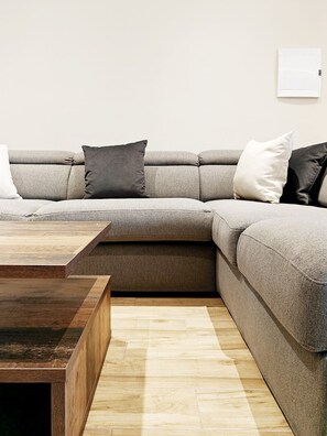 Un salon moderne avec un canapé d’angle, une table basse en bois et un tapis de couleur claire.