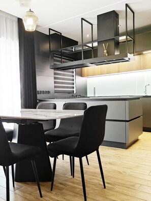 A modern kitchen with a central island, black chairs, and a dining table. - Black Diamond apartment (Żabbar)