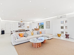 A modern living room with a sectional sofa, a dining area, and a kitchen in the background.
