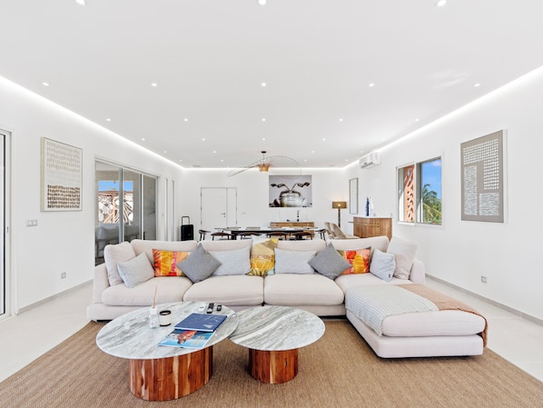 A modern living room with a sectional sofa, two round coffee tables, and a dining area with a kitchen in the background.