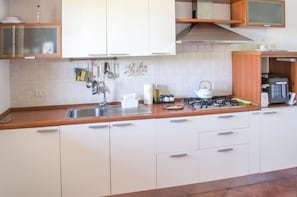 A kitchen with a stainless steel sink, white cabinets, a stove, and various kitchen utensils. - La Casa del Nespolo (Torrita di Siena)