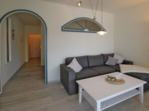 Ein modernes Wohnzimmer mit einem grauen Sofa, einem weißen Couchtisch und einem Fenster mit blauem Rahmen.