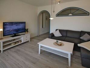 Ein modernes Wohnzimmer mit einem Flachbildfernseher, einem weißen Couchtisch, einem grauen Sofa und einer weißen TV-Konsole.