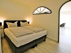 A modern bedroom with a bed, two bedside lamps, and a unique arched window. - 19 Grosse Strasse, Holiday Apartment 1 (Wyk auf Foehr)