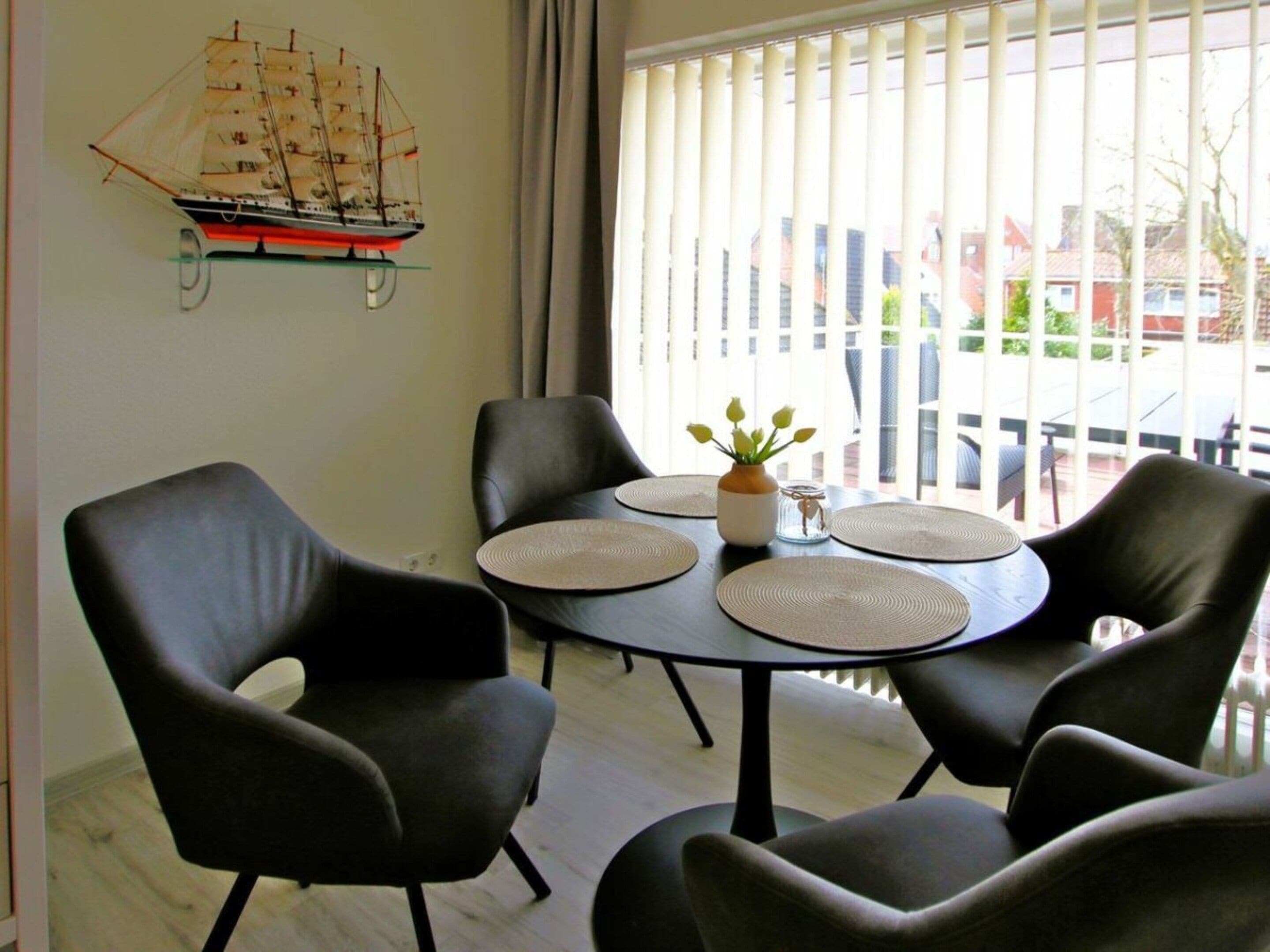 Een eetgedeelte met een ronde tafel, zwarte stoelen en een scheepsmodel aan de wand.