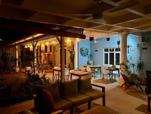 Een binnenzitgedeelte met tafels, stoelen, een houten bank en potplanten.