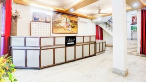 A reception area with a reception desk, a wall-mounted calendar, and a staircase with red curtains. - Collection O Nandanpura Sipri Bazar (Jhansi)