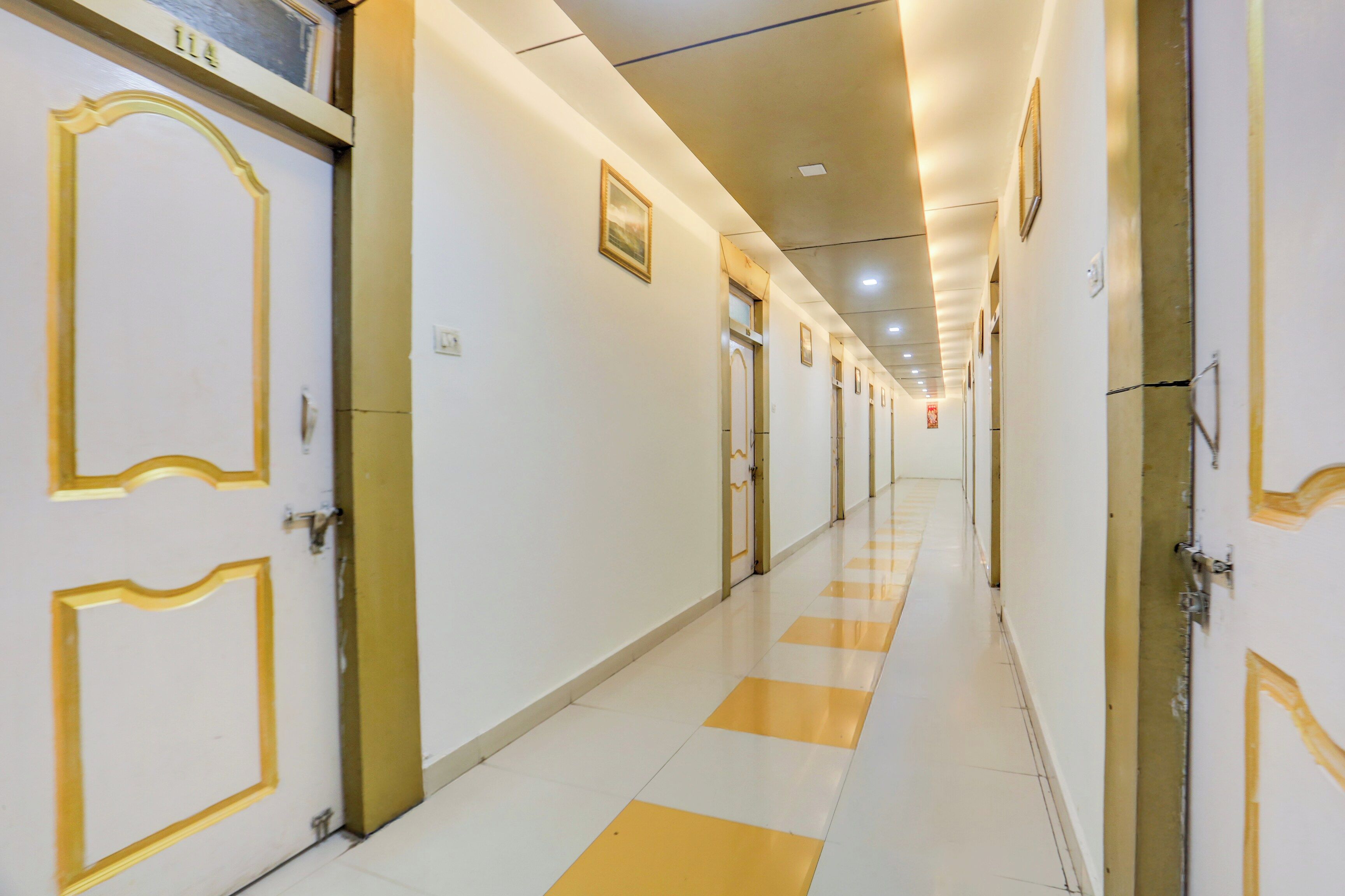 A hotel corridor with doors on both sides, a checkered floor pattern, and a ceiling with recessed lighting.
