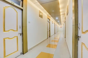 Pasillo de hotel con puertas a ambos lados, un piso con diseño de cuadros y un techo con iluminación empotrada.