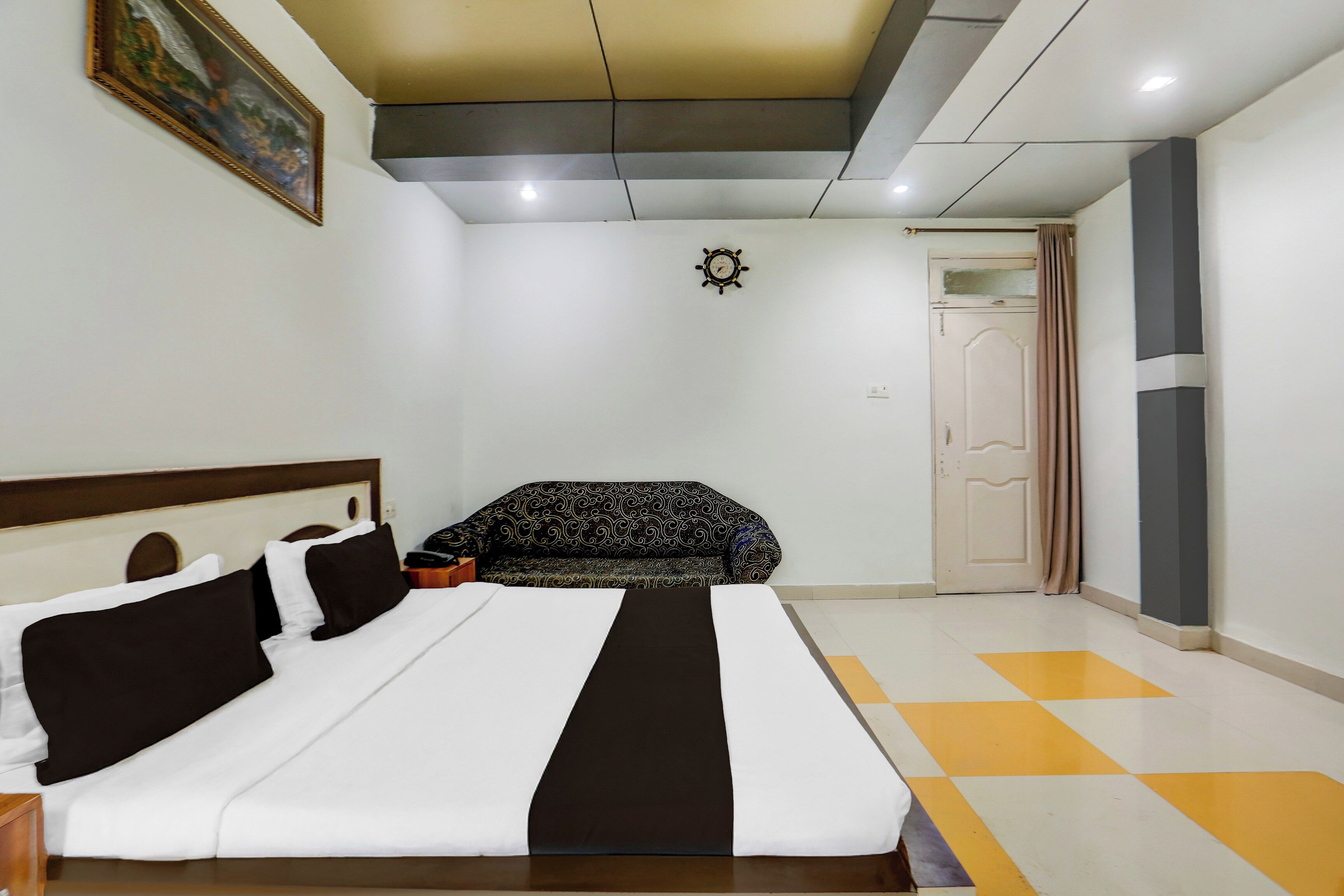 A hotel room with a bed, a sofa, a door, and a wall-mounted clock.