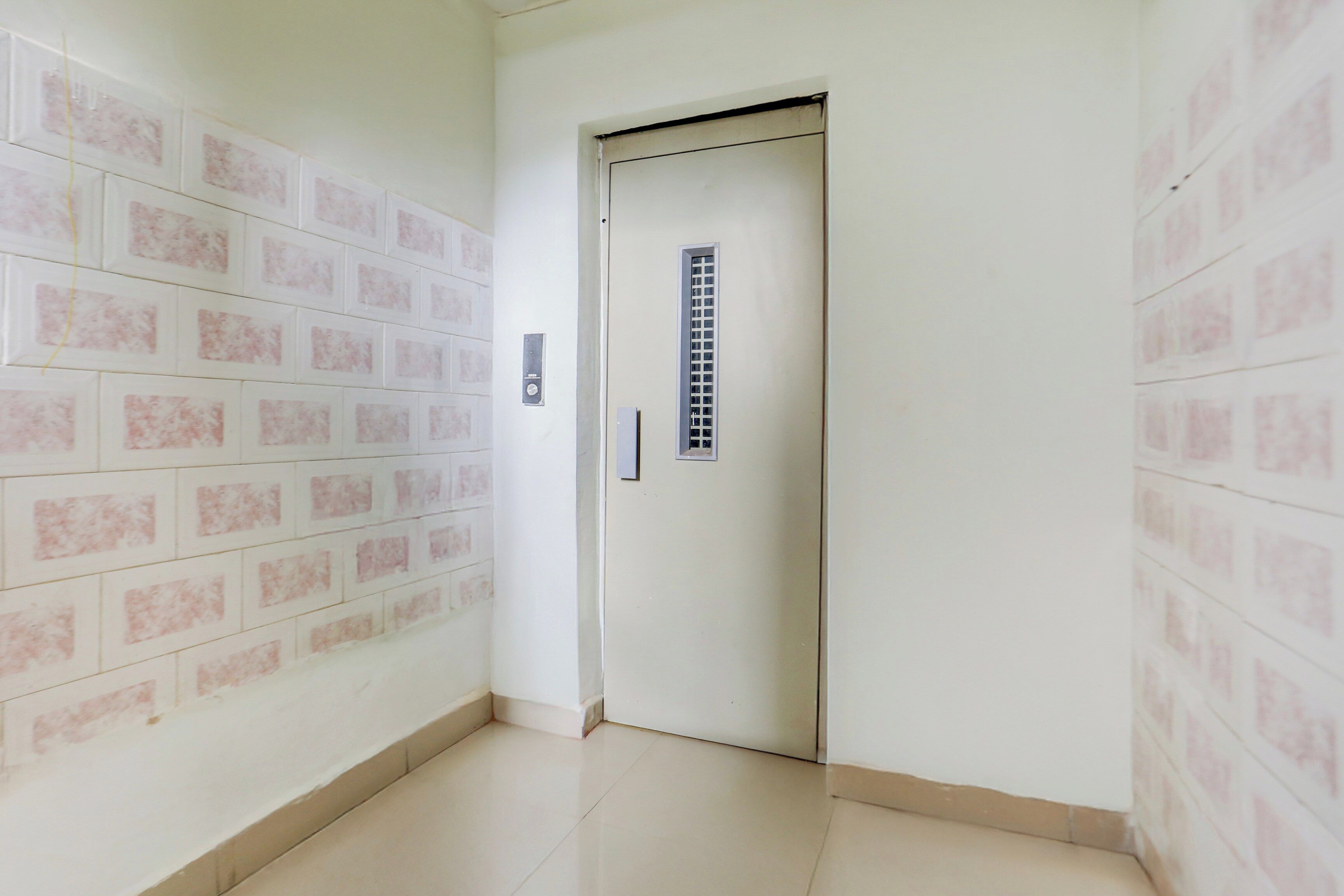 A hallway with a white door and a wall-mounted elevator control panel.