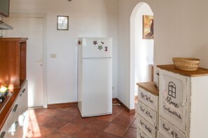 A kitchen with a white refrigerator, wooden cabinets, and a tiled floor. - La Casa del Nespolo - Two-Story Townhouse in Torrita di Siena (Torrita di Siena)