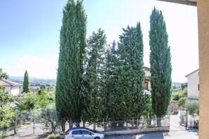 A residential area with tall cypress trees, a parked car, and a building with a tiled roof. - La Casa del Nespolo - Two-Story Townhouse in Torrita di Siena (Torrita di Siena)