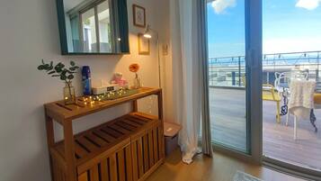 A room with a wooden console table, a mirror, a vase with a flower, and a view of the balcony.