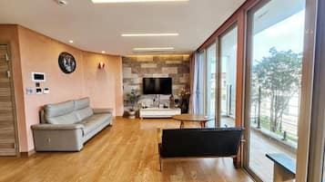A modern living room with a sofa, a bench, a TV, and a large window offering a view.
