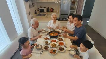 A family dining at a table with various dishes, a kitchen in the background, and a modern interior design.