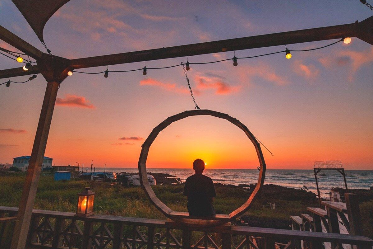 A person sitting in a circular frame overlooking a sunset, with a beach and ocean in the background.