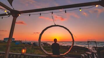 A person sitting in a circular frame overlooking a sunset, with a beach and ocean in the background.