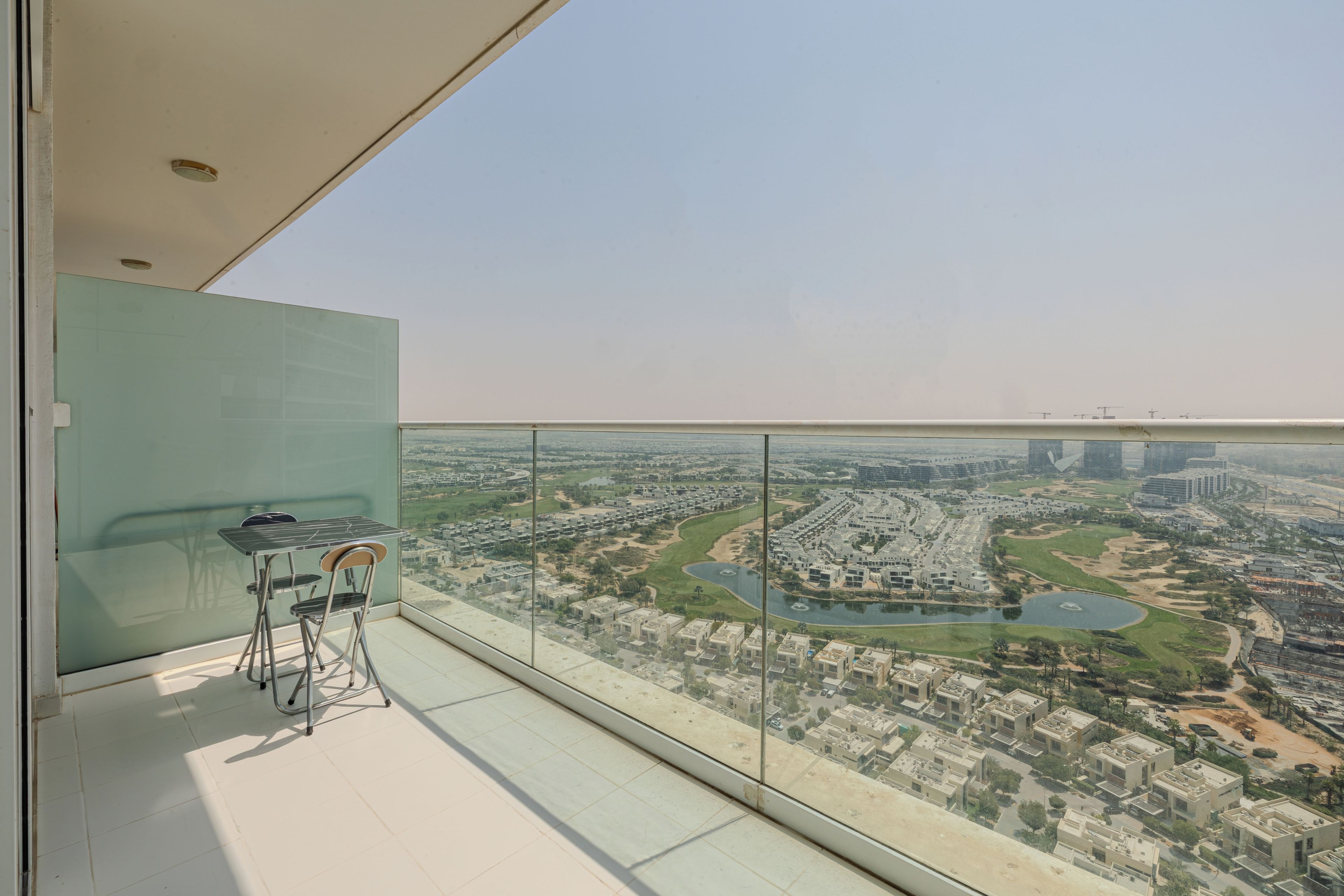 A balcony with a glass railing overlooking a residential area with a river and buildings.