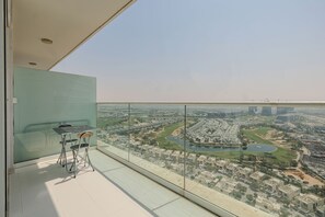 A balcony with a glass railing overlooking a residential area with a river and buildings. - Modern Studio Golf Views DAMAC Hills 1 (Dubai)