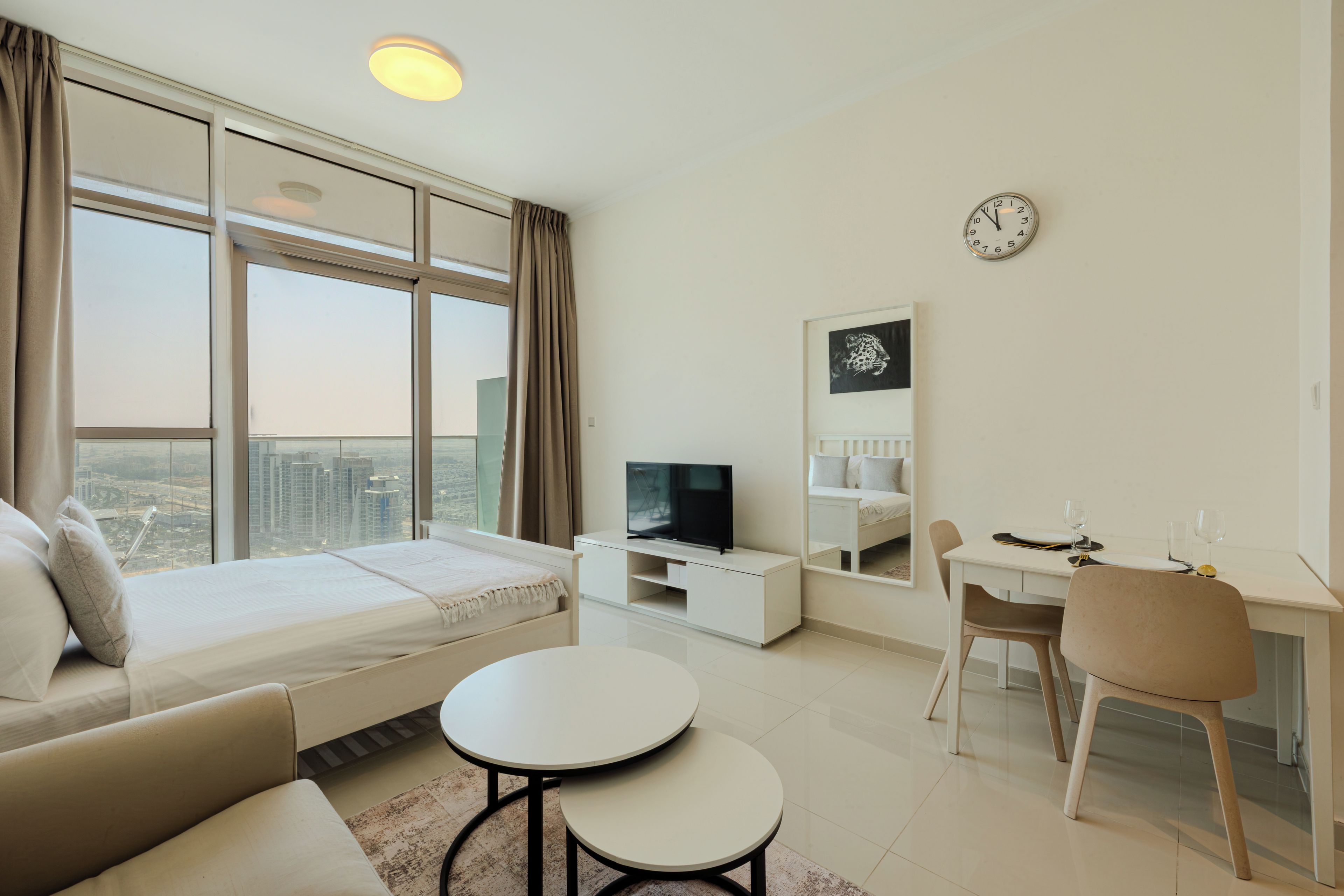 A modern living room with a sofa, a TV, a dining area with a table and chairs, and a large window with curtains.