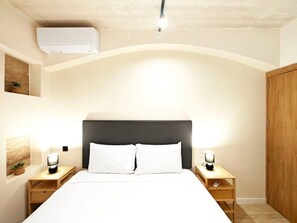 Ein Schlafzimmer mit einem Bett, zwei Nachttischen, einem Wandgerät zur Klimatisierung und einem Holzschrank.